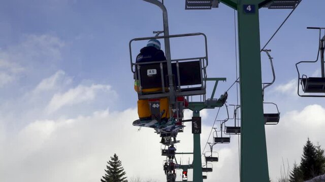 Two young skiers in ski lift elevator going up the mountain on ski slope with lots of snow on cloudy day in winters ports park Austria 50 fps