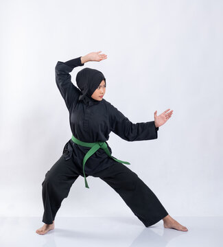 Asian women in hijabs wearing pencak silat uniforms with green belts perform stance movements on the isolated background