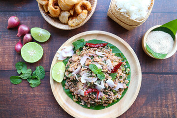 Larb moo - Thai food of spicy minced pork salad with some ingredients served on wood plate - Thai Northeastern traditional local and street food. Top view on the wooden background