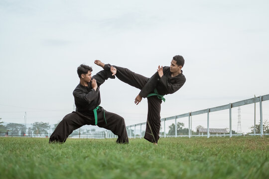 two fighters wearing pencak silat uniforms fighting in an outdoor background
