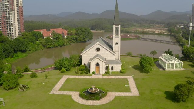 Catholic style church building without a cross surrounded with green grass fields on a bright clear day.. Aerial push back shot.