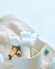 Cup of cocoa with marshmallows and cinnamon on the kitchen tablecloth. Hot chocolate in a white mug. The concept of Christmas and Thanksgiving. Christmas tree toy in the background.