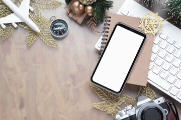 Mockup blank white screen smartphone for Christmas New Year holiday travel background concept on home office desk, Flat lay top view mock up mobile phone with plane model, camera, Xmas ornaments.