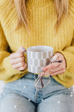 Woman with a warm cup of tea holding her eyeglasses
