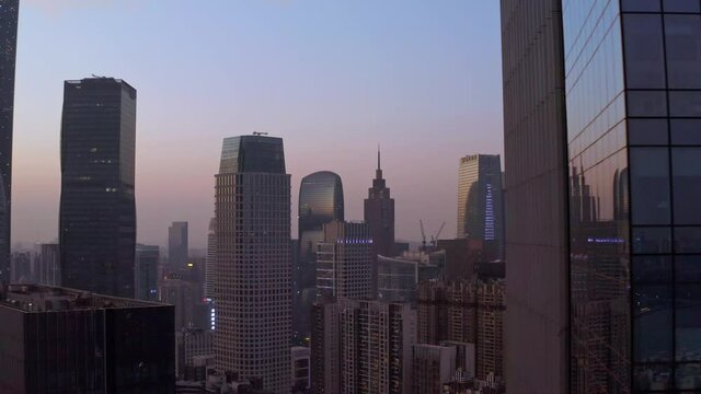 View on Guangzhou downtown CBD office buildings in rays of beautiful colorful sunset. Fly out from behind office building. Aerial shot.