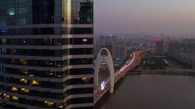 Guangzhou Liede bridge with heavy evening traffic on a beautiful colorful sunset. Pivot from behind office building. Aerial shot.
