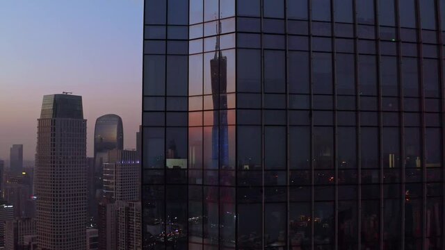Guangzhou Canton tower reflecting in the glass panels of downtown CBD office building on sunset. Aerial descent shot.