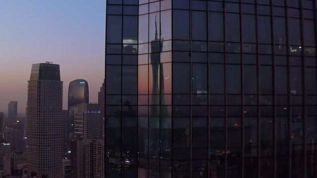 Guangzhou Canton tower reflecting in the glass panels of downtown CBD office building on sunset. Aerial descent shot.