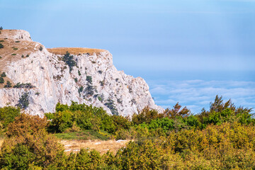High rocky mountains on blue sky background. Green trees on the mountainside.