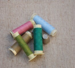 Hilos caqui, rosa, azul y verde de polierter, agujas y dedales metálicos sobre mantel 9
