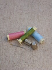Hilos rosa, azul y verde de polierter, agujas y dedales metálicos sobre mantel 7