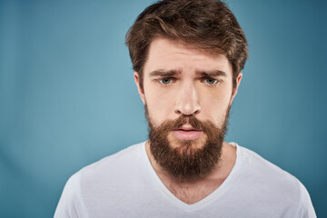 Fototapeta premium Bearded man displeased facial expression emotions close-up blue background white t-shirt