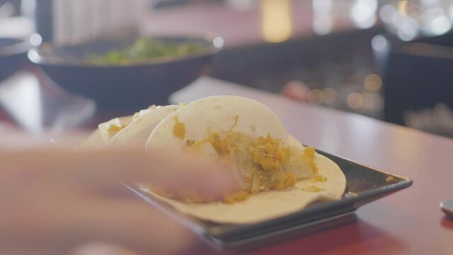 A mexican hard shell tacos with cheese being put on a table with a mexican bowl standing in the background. Shot in 4K.