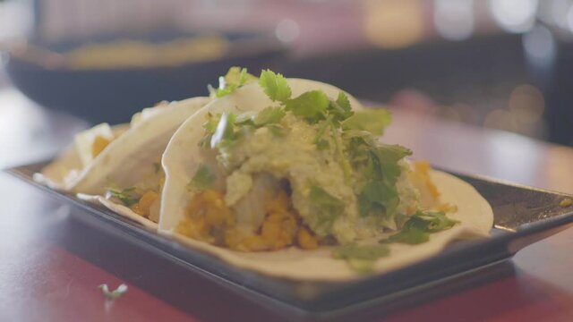 A mexican hard shell tacos with cheese and fresh cilantro being sprinkled on. Shot in 4K. Shallow depth.
