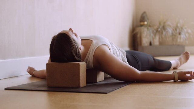 Brunette woman relaxes in Shavasana yoga pose using yoga blocks in studio
