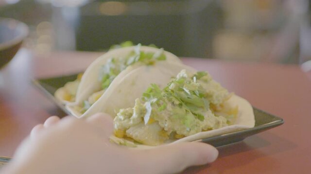 Two mexican hard shell tacos with fresh cilantro being put on a table. Shot in 4K.