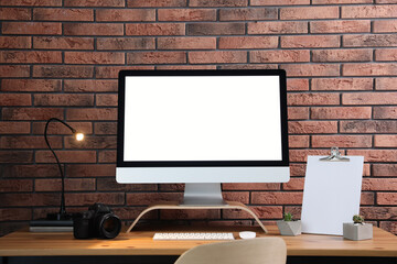 Fototapeta premium Comfortable workplace with modern computer on wooden table near brick wall. Space for text