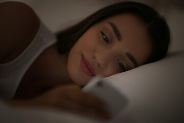 Young woman with nomophobia using smartphone in bed at night. Insomnia concept