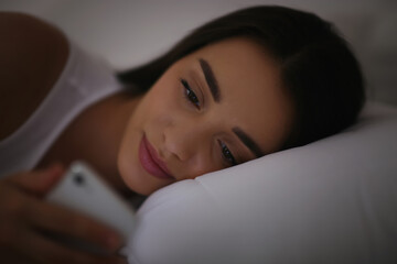 Young woman with nomophobia using smartphone in bed at night. Insomnia concept