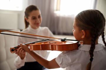 Young woman teaching little girl to play violin indoors