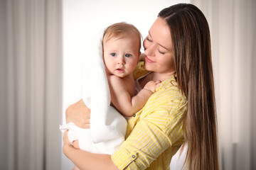 Mother holding cute little baby wrapped with towel indoors after bath