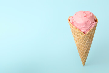 Delicious pink ice cream in waffle cone on light blue background. Space for text