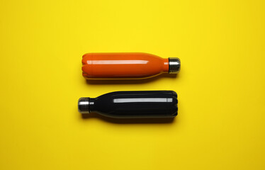 Modern thermo bottles on yellow background, flat lay