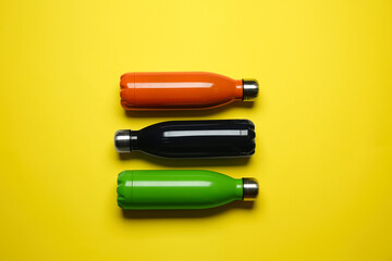 Modern thermo bottles on yellow background, flat lay