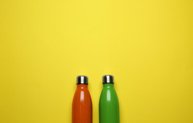 Modern thermo bottles on yellow background, flat lay. Space for text