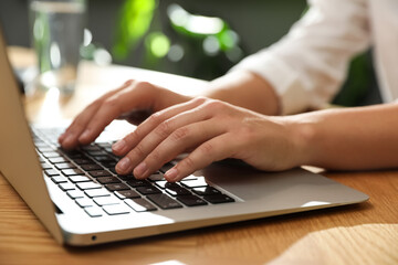 Young woman using laptop for search at wooden table in room, closeup