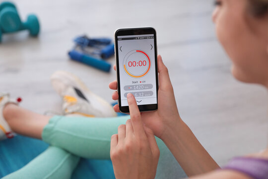 Young Woman Using Fitness App On Smartphone Indoors, Closeup