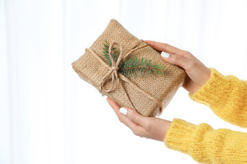 Woman in warm sweater holding Christmas gift on white background, closeup