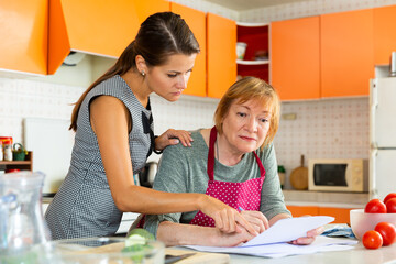 Senior woman with her adult daughter filling out documents at home