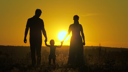 Fototapeta na wymiar little daughter jumping holding hands of dad and mom in park on background of sun. Family concept. child plays with dad and mom on field in sunset light. Walking with small kid in nature. childhood