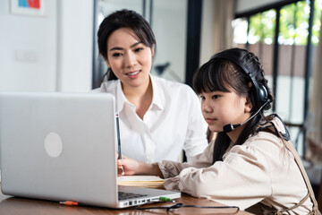 Asian mother teaching daughter learning online class on computer.