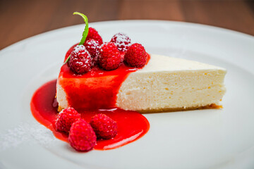 A piece of classic cheesecake new york, raspberry syrup topping, garnished with fresh berries and mint, white plate