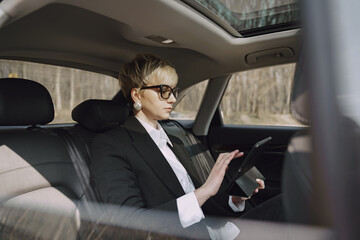 Businesswomanin a car. Lady in a black suit. Woman use a tablet.