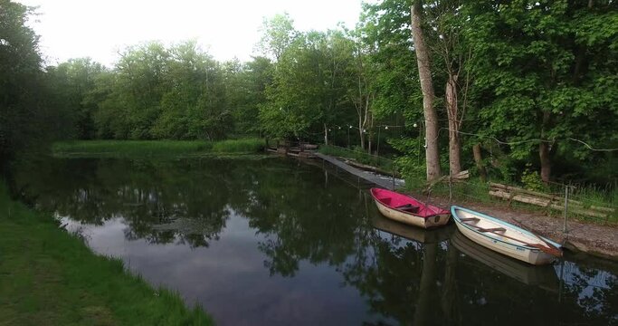 Small Bridge by a Calm River With Two Boats Surrounded by Green Trees in South Sweden Sk&aring;ne &Ouml;sterlen, Nybro&aring;n, Aerial Low Smooth and Slow