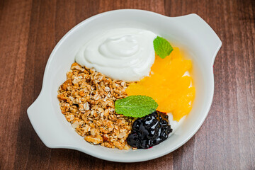 Healthy breakfast, consisting of granola with greek yogurt and fresh orange, berry jam, served in a white plate.
