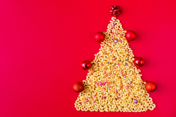 Christmas tree made of raw italian pasta with red balls isolated on red background. Winter holidays concept