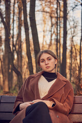 A teenage girl with blonde hair sits on a bench in an autumn Park.