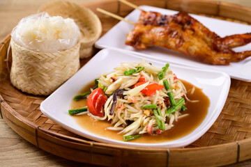 Thai food (Som Tum), Spicy green papaya salad eating with grilled chicken wing and sticky rice on bamboo tray