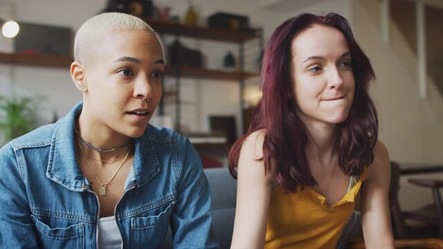 Same sex female couple sitting on sofa at home playing computer game together - shot in slow motion