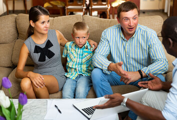 Cheerful family couple with tween son consulting with African-American male real estate agent at home
