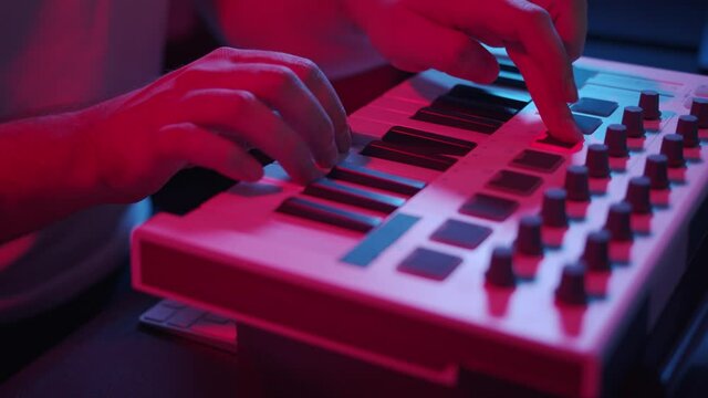 Male hands recording music, playing electronic keyboard, midi keys on the table with neon lights. Closeup of male hands composing music in night using midi controller
