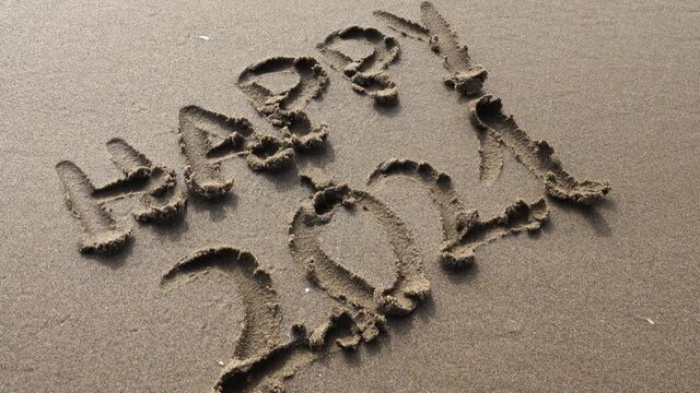 Hand writing happy 2021 in the sand at sunset with beautiful lighting