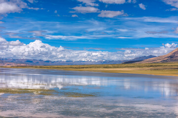 The lake scenery on the plateau, and the snow-capped mountains under the blue sky and white clouds in the distance