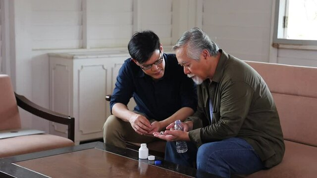 Senior Asian man is taking his congenital disease medicine including hypertension and cholesterol pill from his son at his retirement pension home