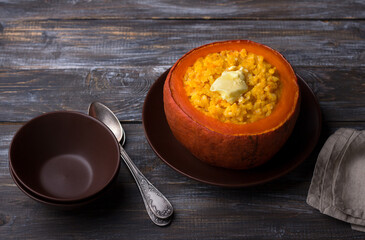 Sweet pumpkin rice with butter baked  in pumpkin pot on a wooden table. delicious seasonal homemade breakfast