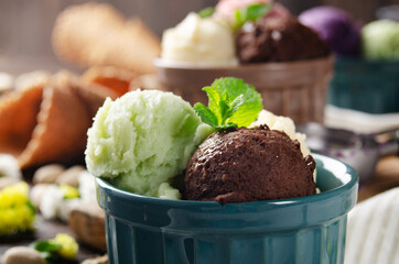 Three scoops of Vanilla pistachio and chocolate icecream balls in clay bowls on wooden kitchen table